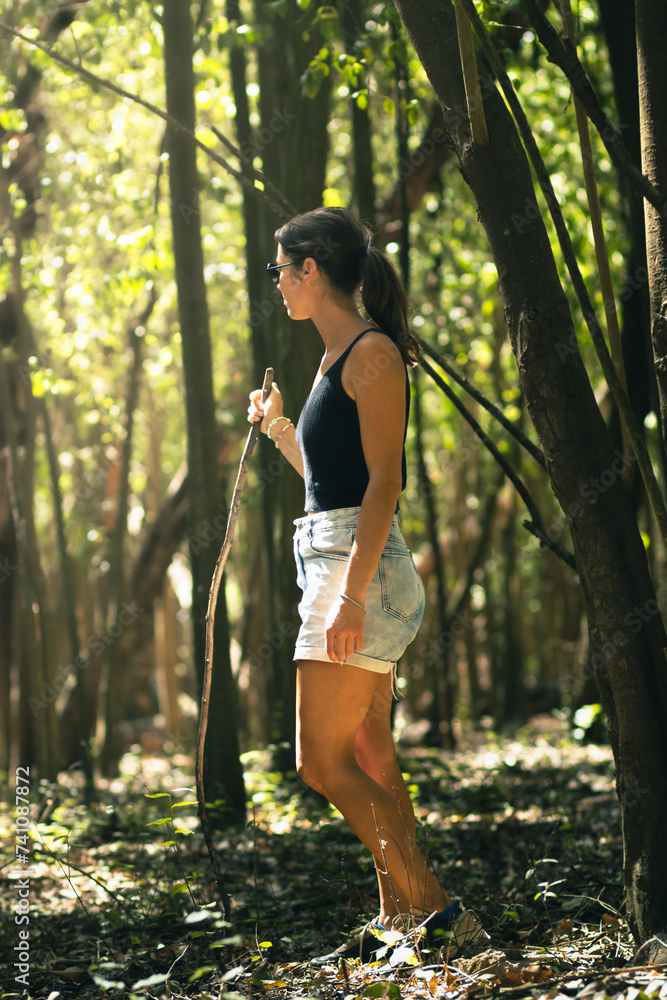 Young woman discovering a forest with a stick in her hand