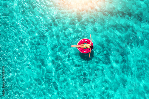 Aerial view of a woman swimming with red swim ring in blue sea