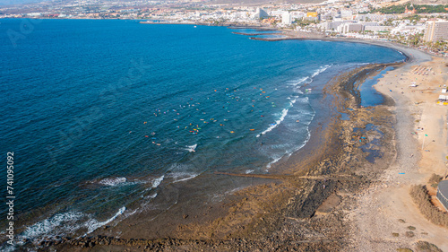 Aerial photo from drone to de surfers in the ocean beachs Adeje Playa de las Americas, Playa Honda In the background Tenerife at sunset. Tenerife, Canary islands, Spain