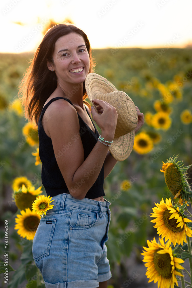 Young smiling woman in a sunflower plantation during golden hour