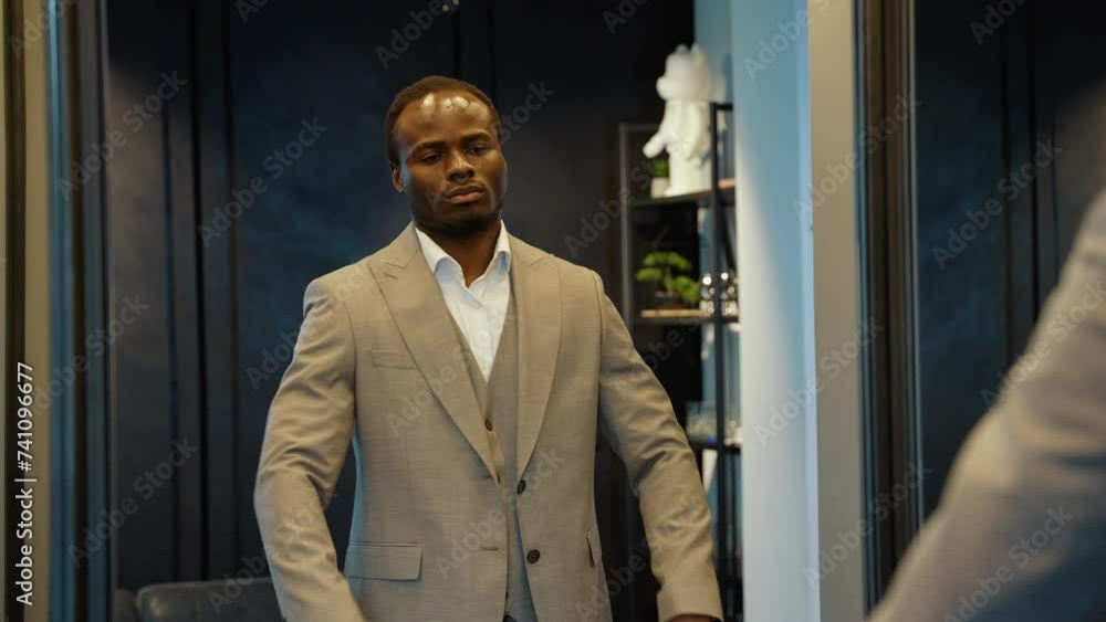 Handsome african american man trying on new suit and looking to mirror in luxury clothing store Handsome african american man trying on new suit and looking to mirror in luxury clothing store