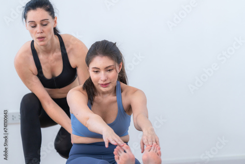 Two women confident training yoga. Athletic women in sportswear doing fitness stretching exercises at home in the living room. Sport and recreation concept. Yoga teacher is helping young woman.