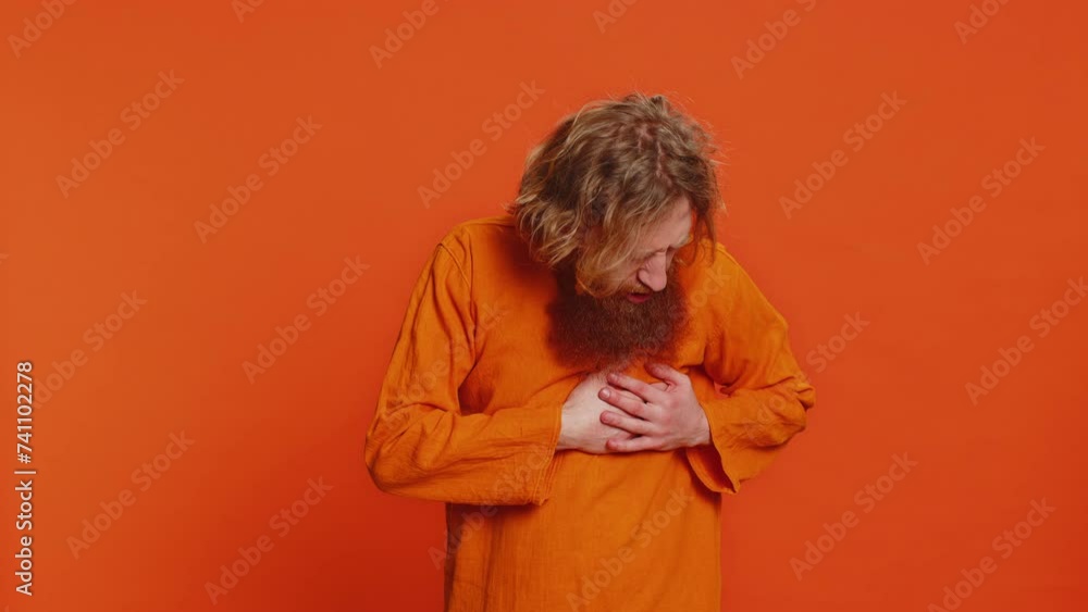 Stressed scared sick ill Caucasian man suffers from tension holding chest with heart pain attack risk of stroke pressure symptom, feeling bad sick ill. Young guy isolated on orange background indoors Stressed scared sick ill Caucasian man suffers from tension holding chest with heart pain attack risk of stroke pressure symptom, feeling bad sick ill. Young guy isolated on orange background indoors