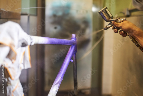 Unknown person spray painting a bicycle frame in his workshop with an airbrush.