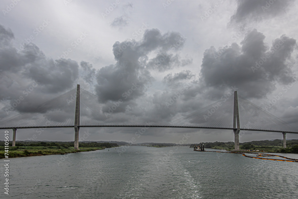 Panama Canal, Panama - July 24, 2023: Atlantic suspension bridge wide panorama just out of Canal under gray cloudscape. Colored pipeline floaters in water, Cutter Suction Dredger Quibian 1
