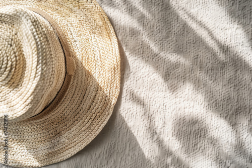 A straw hat on a beach mat under the shadows of a palm leaves. Relaxed summer scene, vacation, sun, sea.