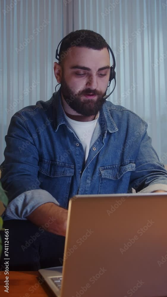 Vertical video. Young adult employee wearing headset having conference video call on laptop. Male professional call center agent, having distance webcam chat. Work from home concept
Vertical video. Young adult employee wearing headset having conference video call on laptop. Male professional call center agent, having distance webcam chat. Work from home concept