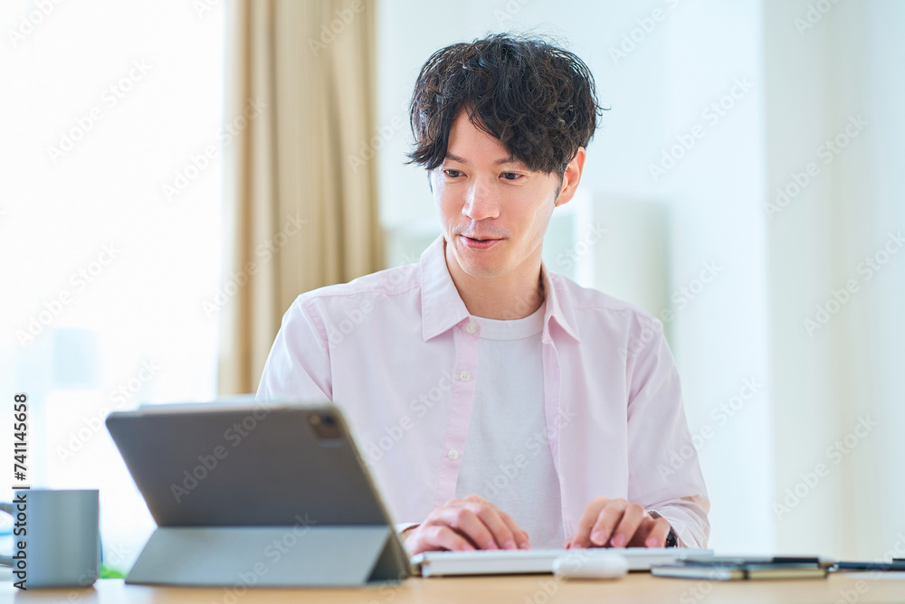 部屋でパソコンの操作をする若い男性 部屋でパソコンの操作をする若い男性