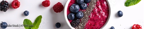 Top view of a nutritious berry smoothie bowl topped with chia seeds, blueberries, and raspberries on a white background. photo