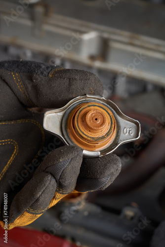 close-up of mechanic holding an old rusty and muddy car radiator cap, rust buildup on vehicle radiator, issues in car cooling system like overheating and corrosion, selective focus with copy space