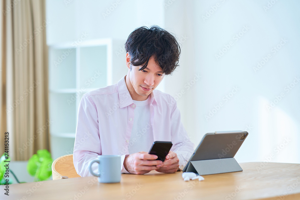 タブレットpcとスマートフォンを見比べる若い男性 タブレットpcとスマートフォンを見比べる若い男性