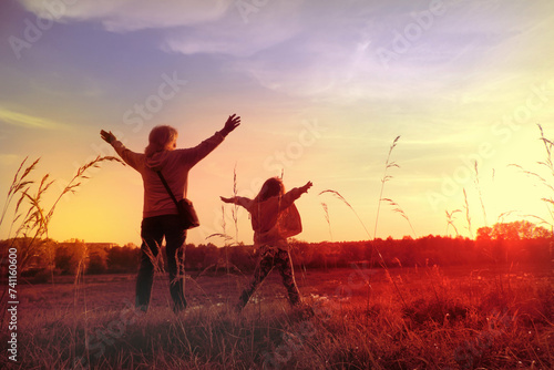 Child girl with mother in the meadow with raised hands, rear view. Relaxing. Summer sunset. Enjoying Life