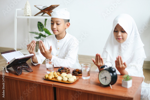 Young Muslim boy and girl praying while waiting for iftar in Ramadan