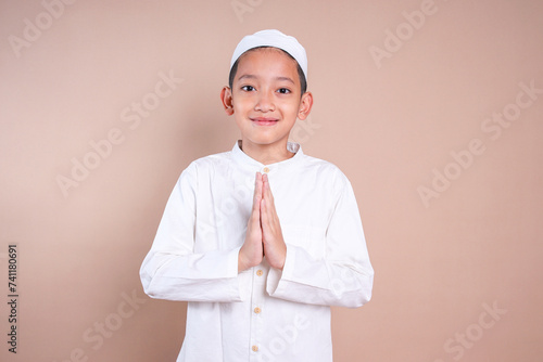 Asian Muslim little boy wear skullcap, showing greeting gesture with happy expression