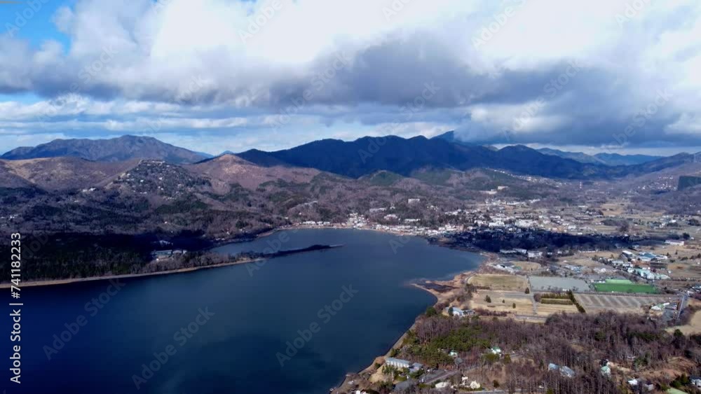 A serene lake with nearby town surrounded by mountains under a cloudy sky, daytime, aerial view A serene lake with nearby town surrounded by mountains under a cloudy sky, daytime, aerial view