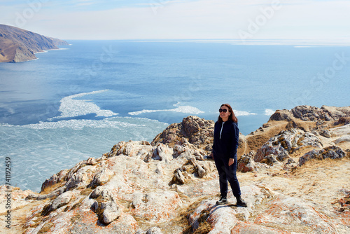 Lake Baikal in spring. The girl stands on a rock with and enjoys the beautiful landscape. Ice melting time. The concept of freedom, travel. photo