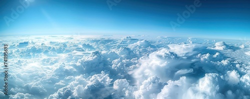 A stunning aerial panorama of dense cumulus clouds bathed in sunlight, with a clear blue sky above.