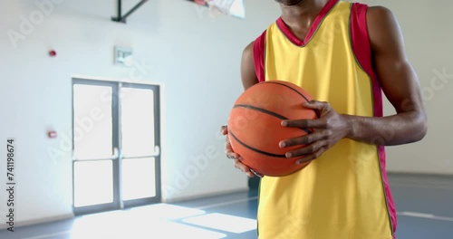 Young African American man holds a basketball in a gym, with copy space photo