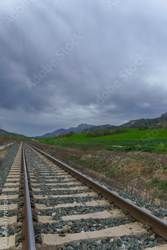 train track with mountainous landscape in the background and stormy cloudy sky