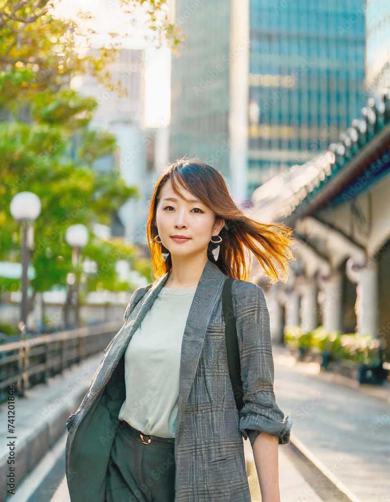 Fototapeta premium 都会のビジネス街を、スーツを着て颯爽と歩く若いアジア人女性。