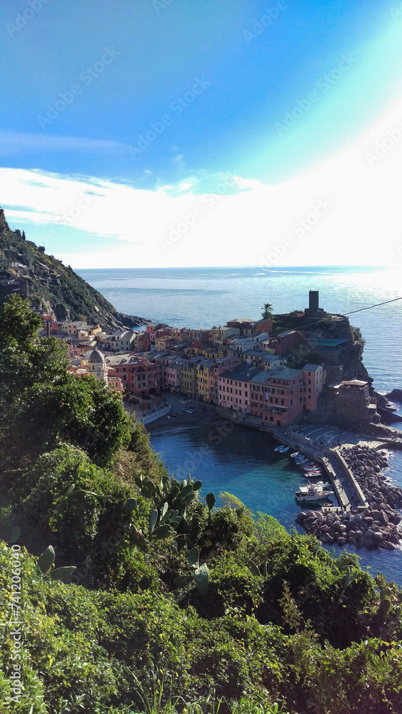 Coastal Italian village with terracotta roofs, nestled between green hills and the blue sea, under a clear sky.