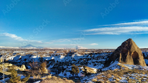 A panoramic view of a snowy landscape with rock formations and clear blue sky.