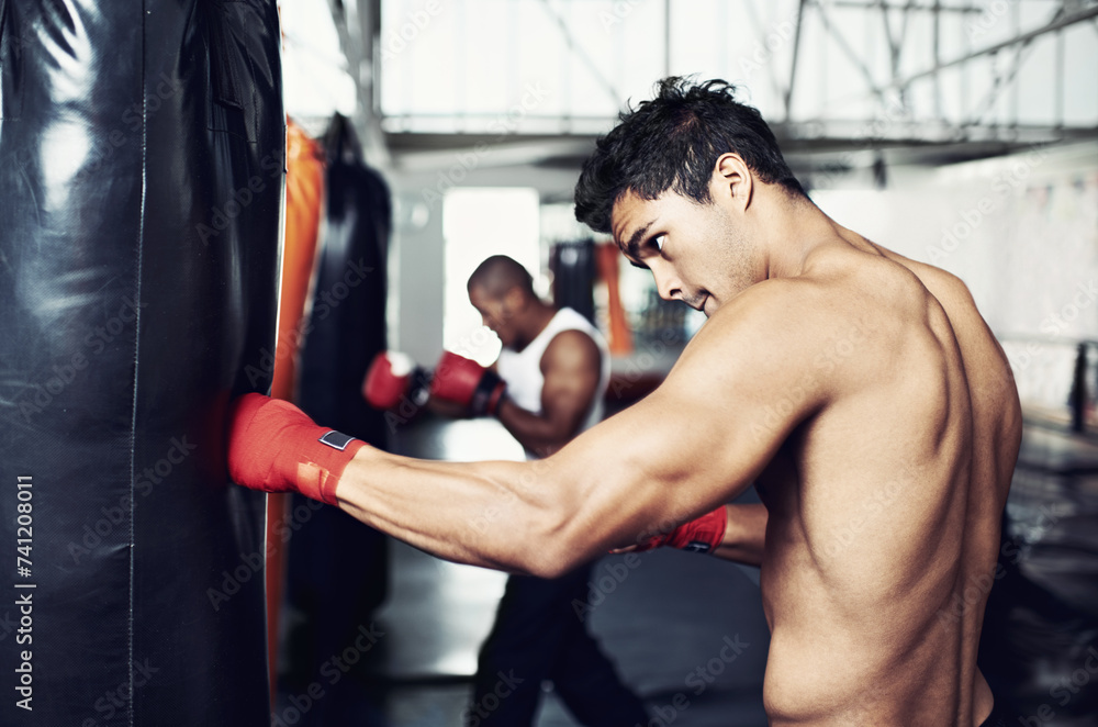 Fitness, punching bag and man with boxing gloves at a gym for training, resilience or performance. Sports, body and male boxer profile with punch practice for strength, energy for fighting exercise