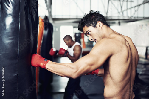 Fitness, punching bag and man with boxing gloves at a gym for training, resilience or performance. Sports, body and male boxer profile with punch practice for strength, energy for fighting exercise © Mariusz/peopleimages.com