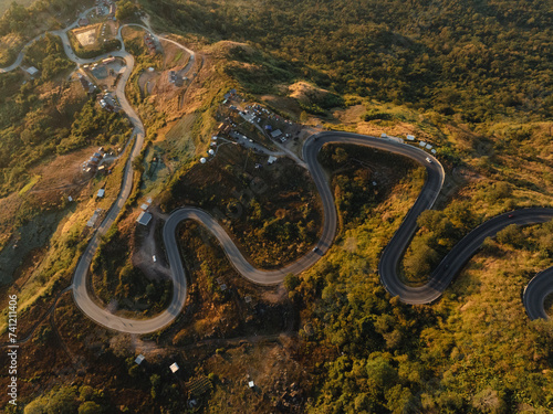 Aerial view of serpentine roads slicing through the rugged terrain of a mountain, illuminated by the warm glow of the setting sun.