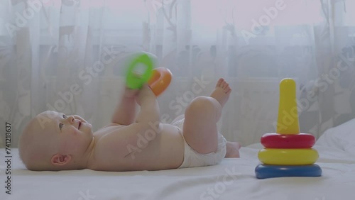 Infant in white diaper on back hold rings, playful discovery, colorful toy, bedroom setting, development play. Baby focus on motor skill, playtime learn, engage with education pyramid toy, child Smile