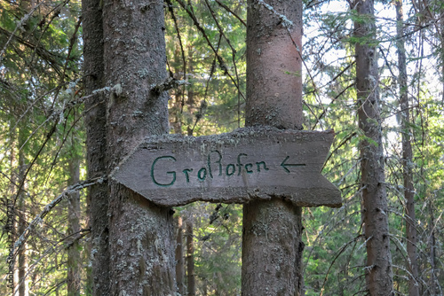 Directional path sign leading to unique rock formations Grossofen surrounded by idyllic forest in Modriach, Hebalm, Kor Alps, border Carinthia Styria, Austria. Wooden board fixed on large tree photo