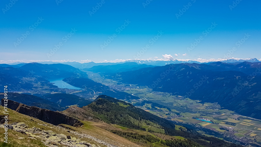 Idyllic hiking trail on alpine meadow with scenic view of lake Millstatt seen from mountain peak Boese Nase in Ankogel Group, Carinthia, Austria. Remote landscape in majestic Austrian Alps in summer