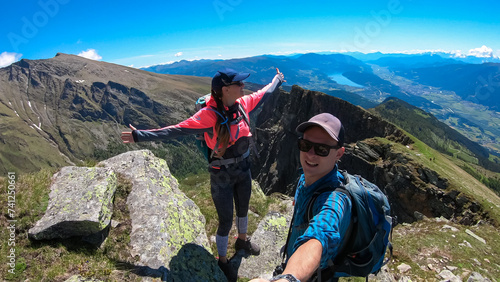 Hiker couple on alpine meadow with scenic view of lake Millstatt seen from mountain peak Boese Nase, Ankogel Group, Carinthia, Austria. Remote landscape. Idyllic hiking trail Austrian Alps in summer