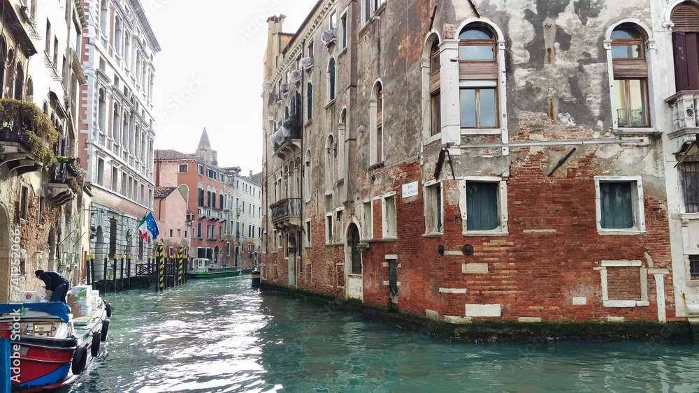A Venice canal with weathered buildings and moored boats, reflecting the charm and history of the city's unique aquatic urban infrastructure.