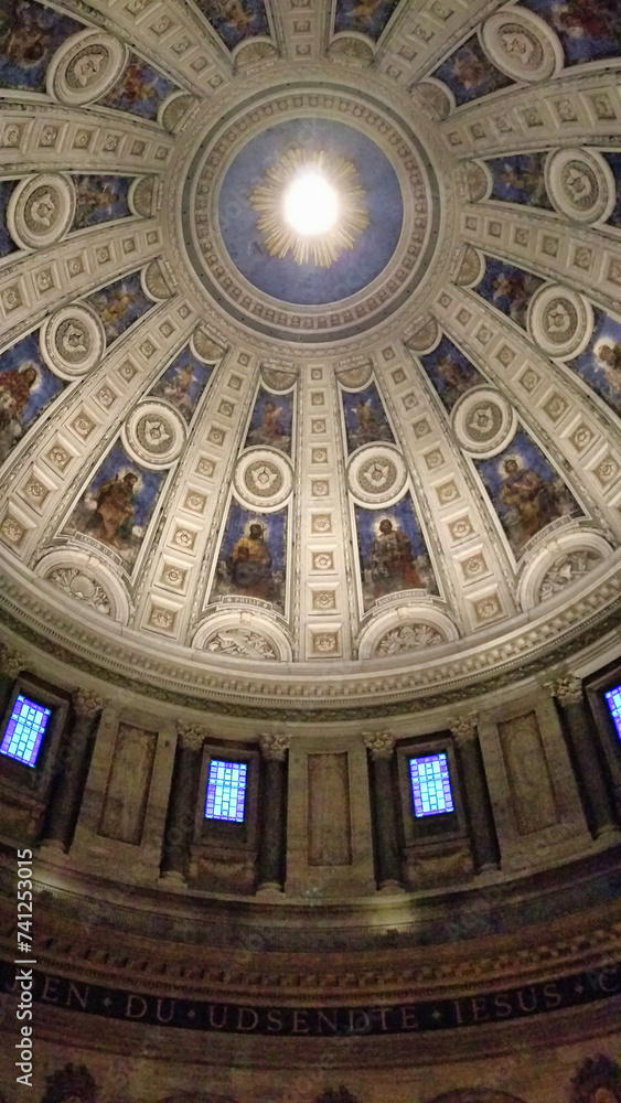 The ornate dome interior of a grand building with elaborate frescoes, coffered detailing, and streaming light from the oculus at the top, symbolizing art and history.