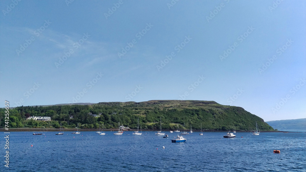 A serene bay scene with a hillside backdrop, showing calm waters, clear skies, and distant homes amidst greenery, emanating a tranquil atmosphere.