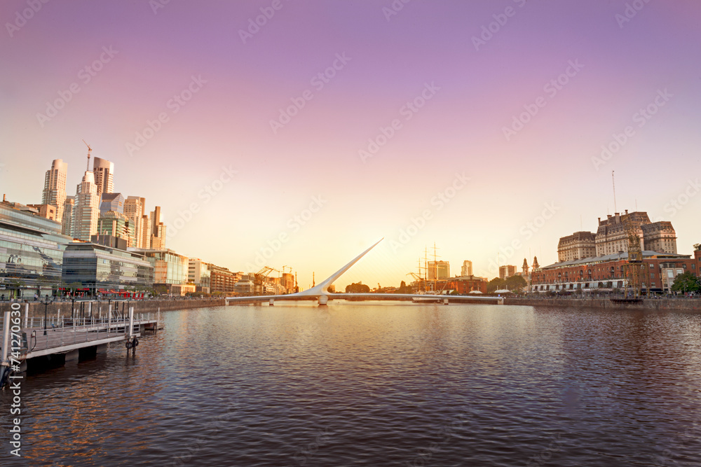 Sunset at Puerto Madero, Buenos Aires, Argentina. The sun sets behind the Puente de la Mujer, casting soft yellows and magentas across the sky, creating an enchanting scene over the Río de la Plata.