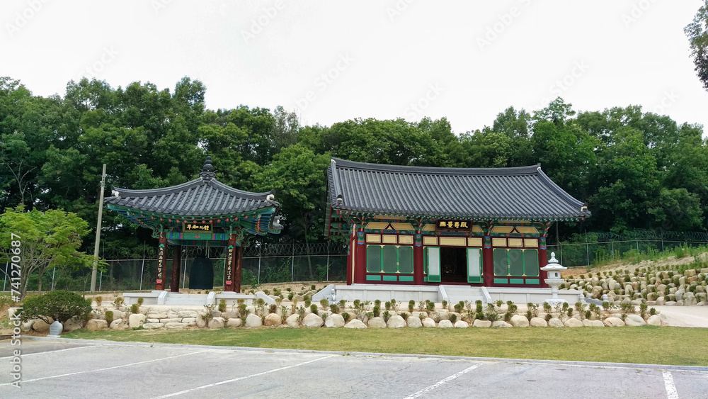 A traditional Korean pavilion set against a backdrop of trees and a stone wall.