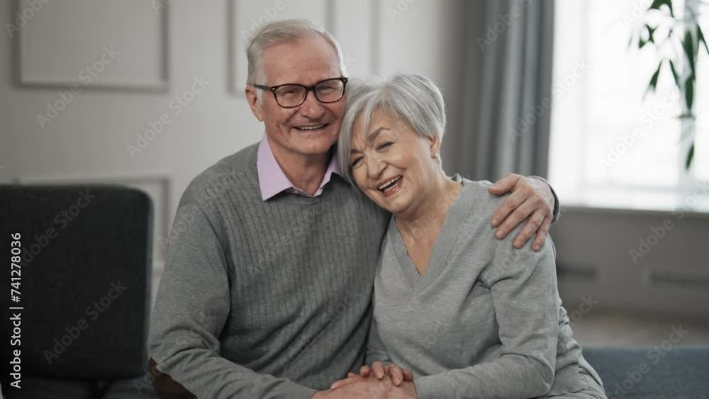 Senior couple holds hands and laughs. Old happy smiling man woman sitting on sofa, hugging and talking. Elderly affectionate spouses wife husband. Love romantic relationships lifelong marriage. Senior couple holds hands and laughs. Old happy smiling man woman sitting on sofa, hugging and talking. Elderly affectionate spouses wife husband. Love romantic relationships lifelong marriage.