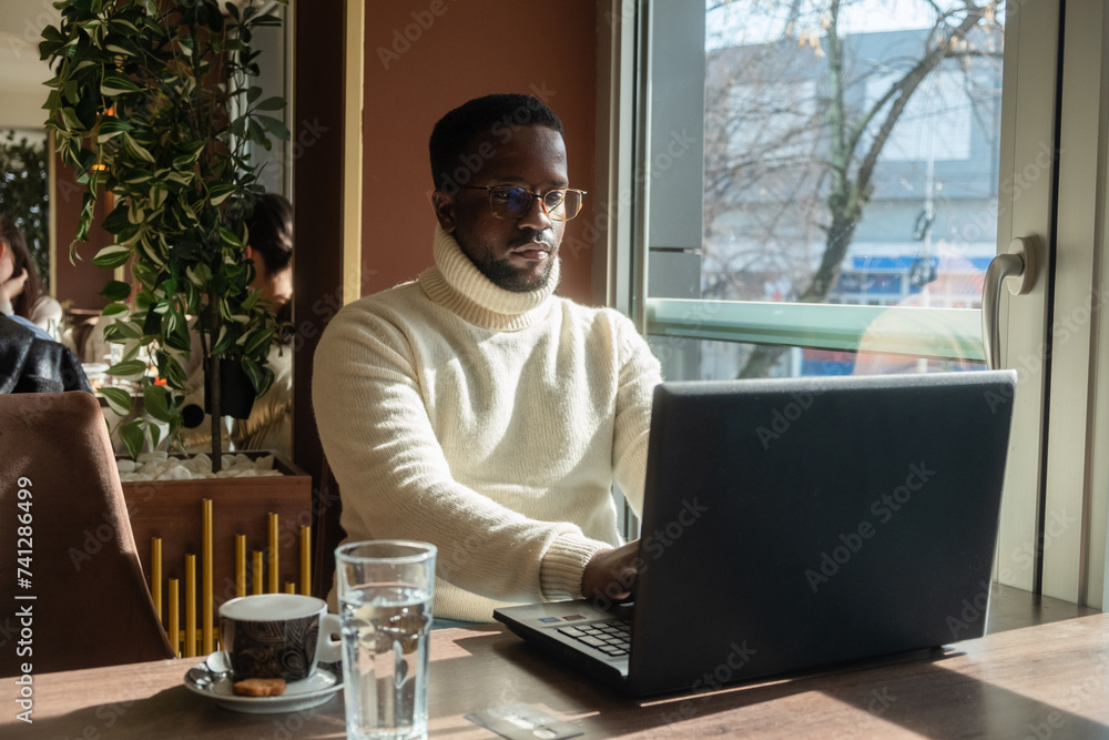 Young black man freelancer working on a laptop in a cafe Young black man freelancer working on a laptop in a cafe