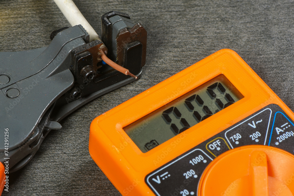 Wire stripper, electrical cable and multimeter on gray workbench background close up. Wire stripper, electrical cable and multimeter on gray workbench background close up.