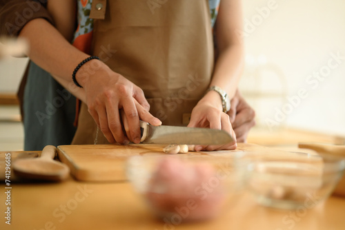 Woman in apron chopping garlic on wooden board, couple preparing food meal in the kitchen