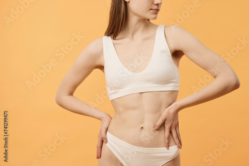 Horizontal crop shot of young Caucasian woman in comfortable underwear posing for camera with hands on hips in studio