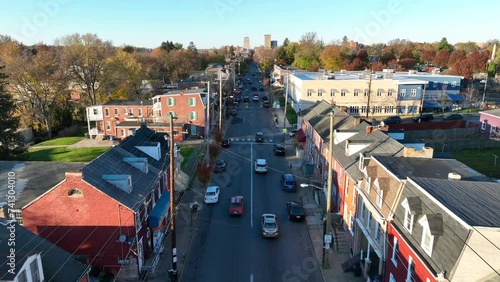 One way street lined with row houses headed towards American city during autumn. Aerial tracking shot above road.