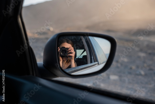 chica sacándose un retrato en el reflejo del espejo retrovisor del coche durante las vacaciones, con una cámara de fotos