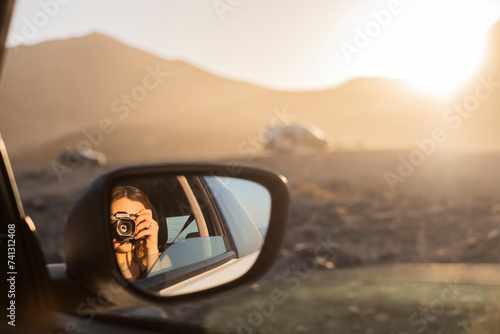 chica sacándose un retrato en el reflejo del espejo retrovisor del coche durante las vacaciones, con una cámara de fotos