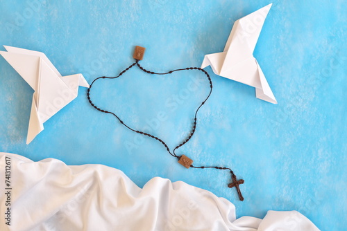 White dove origami carrying rosary or scapular in sky blue background.