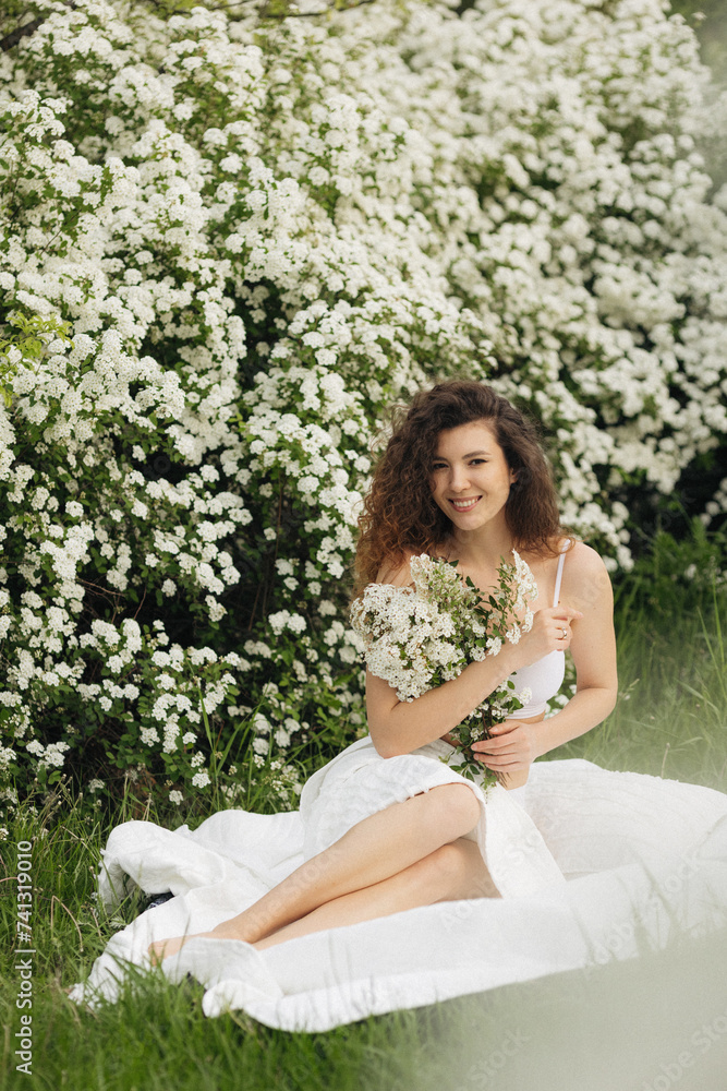Beautiful caucasian curly women smiles in nature in beautiful white flowers