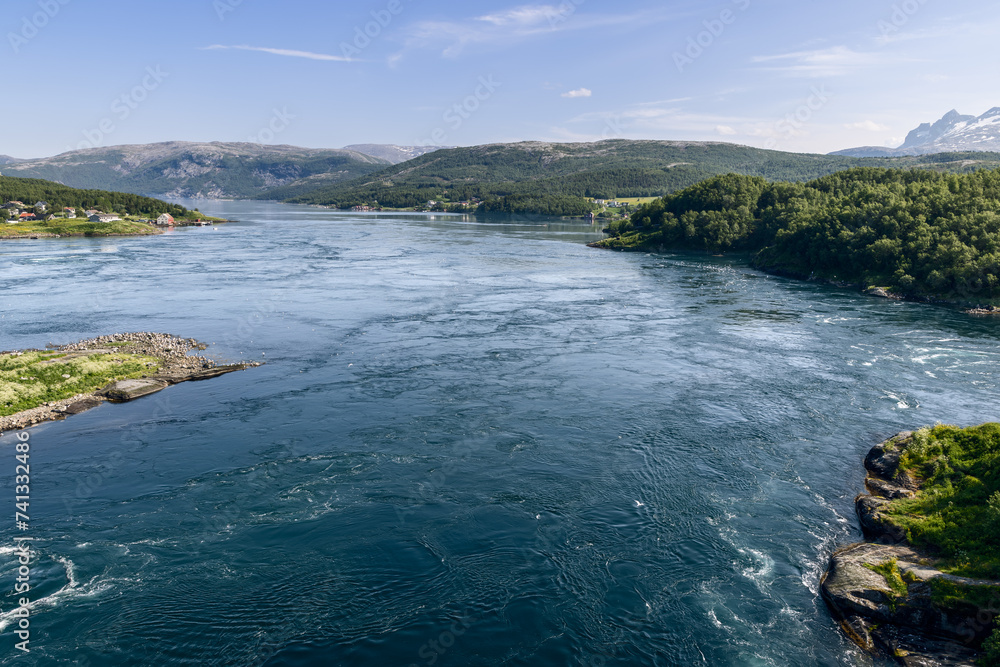 Fototapeta premium The dynamic Saltstraumen tide, captured from above, with its powerful whirlpools contrasting against the serene Nordic scenery and residential areas