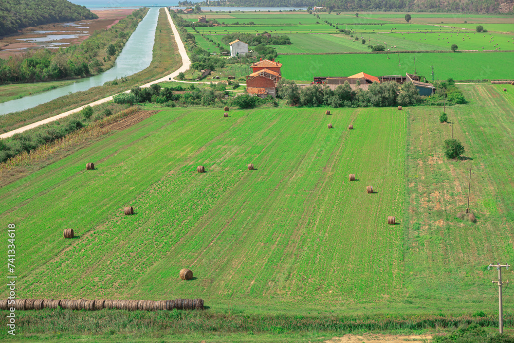 Rural landscape with haystacks in the field and village in the background. Wonderful farmland in the spring. Green agricultural fields in Croatia